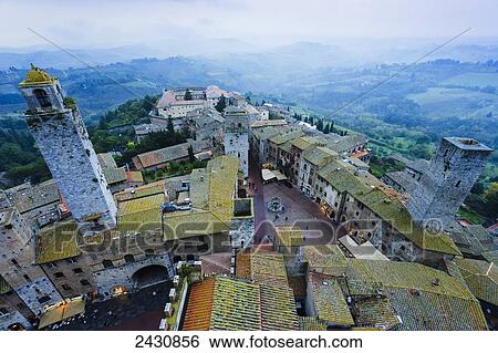 Stock Photograph - Fog covers the distant hills with a high angle view of the city; San Gimignano, Tuscany, Italy. Fotosearch