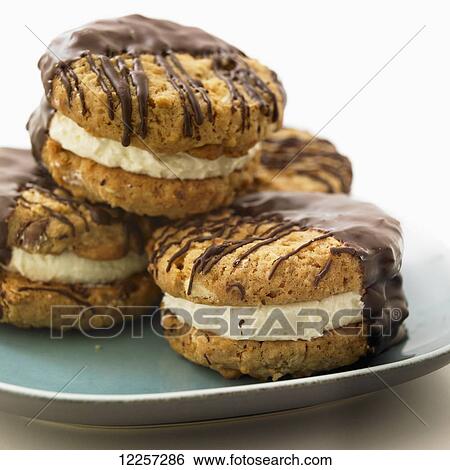 Stock Photograph - Four chocolate dipped sandwich cookies stacked on a teal plate; Victoria, British Columbia, Canada. Fotosearch