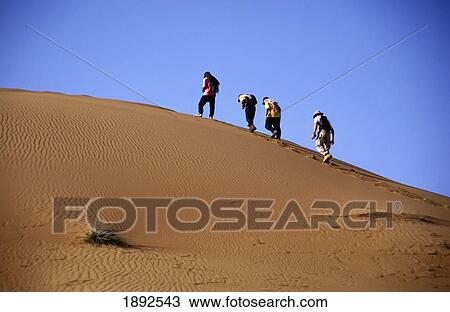 Stock Image - Four People Hiking In Desert Near Al-Ain. Fotosearch
