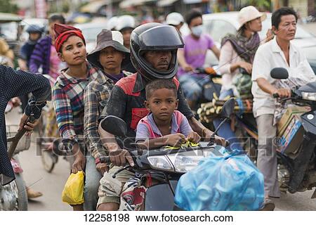 Stock Photo - Four people on a motorbike on a busy street outside Luh Market; Siem Reap, Cambodia. Fotosearch