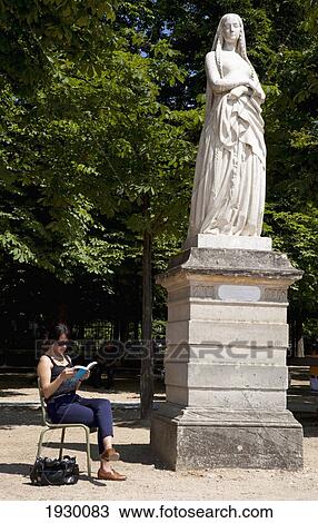 Stock Image - France, The Luxumberg Gardens; Paris, Woman sitting in garden and reading book. Fotosearch