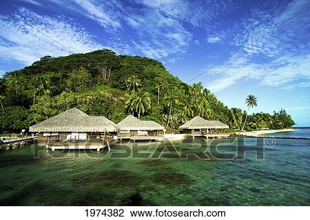 Stock Image - French Polynesia, Huahine, Te Tiare Resort Bungalows Over Ocean, Tall Palm Trees Along Beach, Blue Sky. Fotosearch