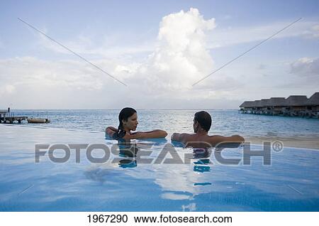 Stock Image - French Polynesia, Moorea, Couple Relaxing In Oceanside Resort Pool.. Fotosearch