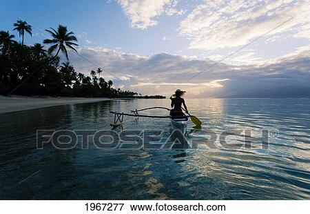 Stock Photo - French Polynesia, Moorea, Woman Paddling In Outrigger Canoe Along Shoreline.. Fotosearch