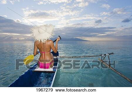 Stock Photo - French Polynesia, Moorea, Woman Paddling In Ocean In Outrigger Canoe.. Fotosearch