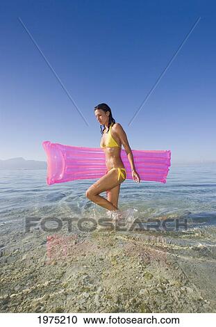Stock Image - French Polynesia, Moorea, Woman Walking Through The Water While Holding Pink Raft.. Fotosearch