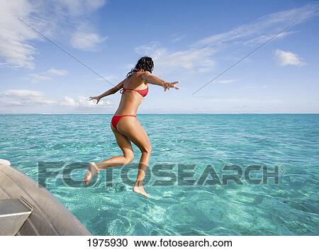 Stock Image - French Polynesia, Moorea, Young Woman Leaps Into The Ocean.. Fotosearch