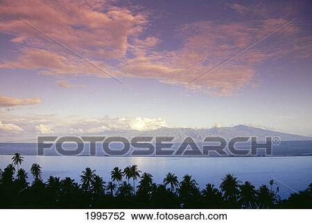 Stock Image - French Polynesia, Papeete, Tahiti From Moorea At Dusk, Island In Distance, Palm Trees And Pin Clouds. Fotosearch