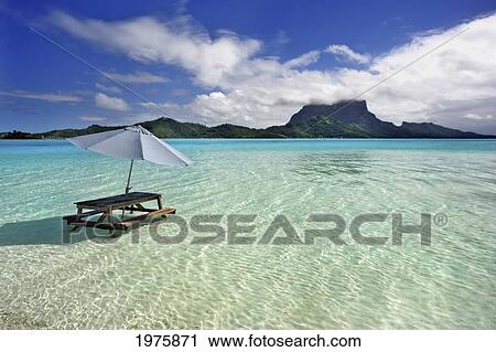 Stock Image - French Polynesia, Tahiti, Bora Bora, Picnic Table And Umbrella In Clear Lagoon Water.. Fotosearch