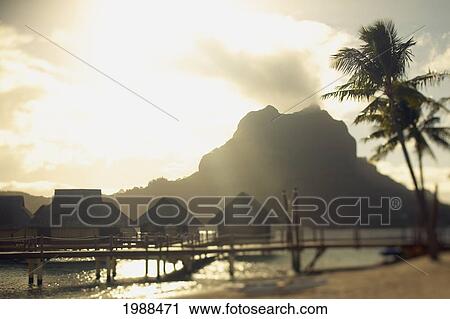 Stock Image - French Polynesia, Tahiti, Bora Bora, Mount Otemanu And Overwater Bungalows At Sunrise. Fotosearch