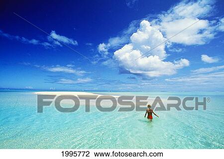 Stock Image - French Polynesia, Tahiti, Bora Bora, Calm Turquoise Ocean Surrounds Sand Islet, Woman Wading, View From Behind. Fotosearch
