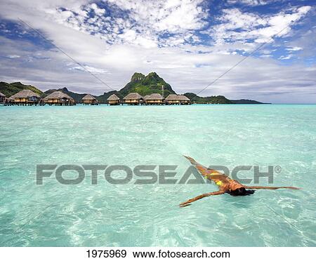 Stock Photo - French Polynesia, Tahiti, Bora Bora, Woman Floating In Water Near Resort.. Fotosearch