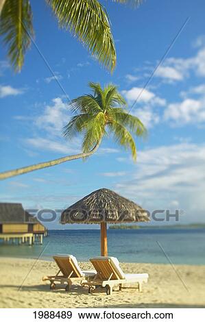 Stock Photo - French Polynesia, Tahiti, Bora Bora, Lounge Chairs And Thatch Umbrella On Beach With Tranquil Ocean And Bungalows. Fotosearch