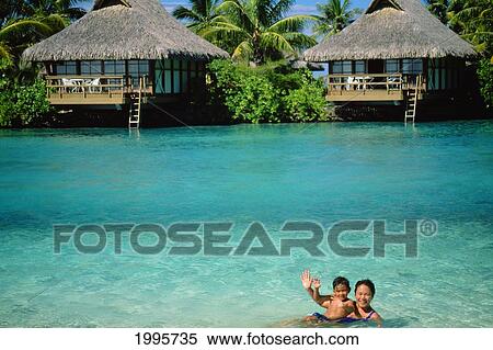 Stock Photography - French Polynesia, Tahiti, Hotel Park Royal Bungalows Over Turquoise Ocean, Mother And Son Waving And Smiling. Fotosearch