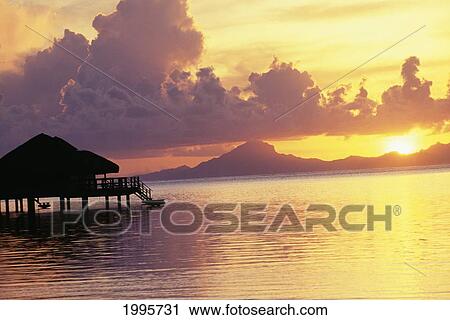 French Polynesia, Tahiti, Huahine, Te Tiare Resort Bungalow Over Ocean, Golden Sunset With Reflections, Raiatea In Background View Large Photo Image Stock Image - French Polynesia, Tahiti, Huahine, Te Tiare Resort Bungalow Over Ocean, Golden Sunset With Reflections, Raiatea In Background. Fotosearch