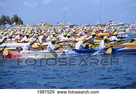 Stock Photo - French Polynesia, Tahiti, Many Men Paddling Canoes At Start Of Race, Escort Boats In Background. No Model Release. Fotosearch