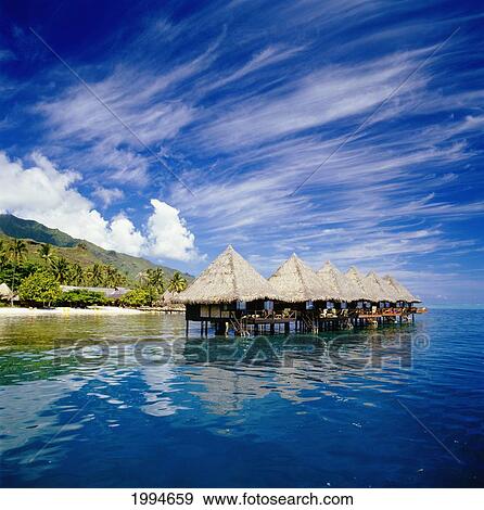 Stock Photo - French Polynesia, Tahiti, Moorea, Bali Hai Resort Huts Over Water, Wispy Clouds In Blue Sky. Fotosearch