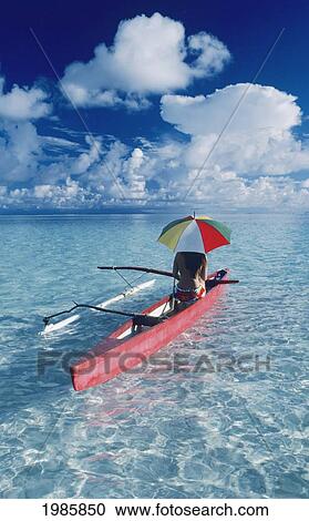 Stock Image - French Polynesia, Tetiaroa, Local Woman In Outrigger Canoe With Umbrella, View From Behind.. Fotosearch