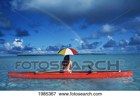 Stock Photo - French Polynesia, Tetiaroa, Woman With Umbrella In Outrigger Canoe Floating On Clear Turquoise Ocean, View From Behind.. Fotosearch