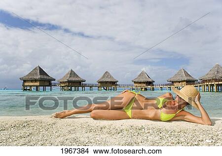 French Polynesia, Tuamotu Islands, Rangiroa Atoll, Woman Lounging On Beach, Luxury Resort Bungalows In Background. View Large Photo Image Picture - French Polynesia, Tuamotu Islands, Rangiroa Atoll, Woman Lounging On Beach, Luxury Resort Bungalows In Background.. Fotosearch