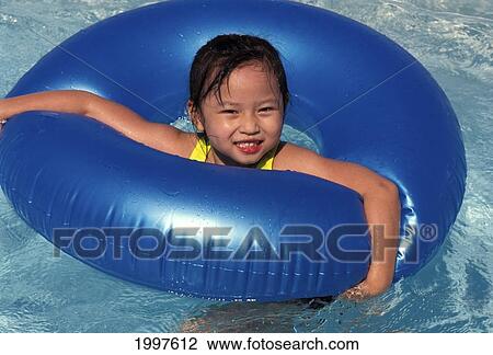 Stock Image - Front View Of Smiling Asian-American Girl Using Large Blue Innertube, Floating. Fotosearch