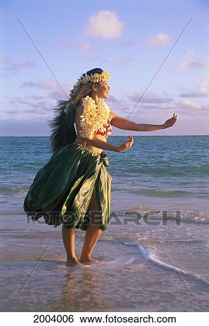 Stock Photograph - Full Length View Of Woman Hula Dancing Along Shoreline Ti-Leaf Skirt And Plumeria Lei. Fotosearch
