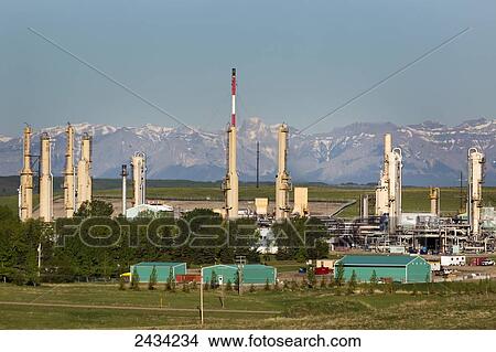 Picture - Gas plant with towers and mountains in the background with blue sky; Alberta, Canada. Fotosearch