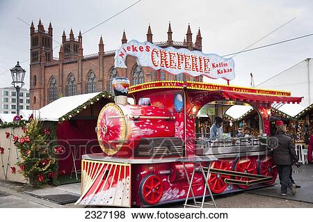 Stock Photo - Germany, drink and gifts. Christmas Markets; Berlin, St Hedwigs Catherdral in background. stall in shape of a steam train stalls selling festive food. Fotosearch
