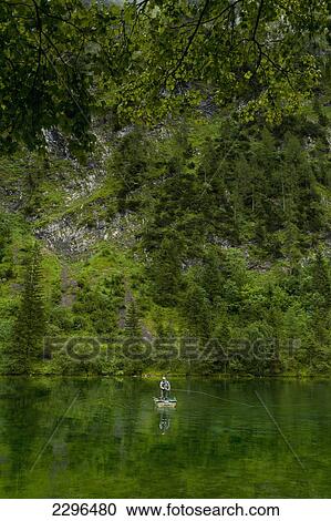Stock Image - Germany, Man fly fishing from small boat in Lake Forggensee near Ruhpolding; Bavaria. Fotosearch