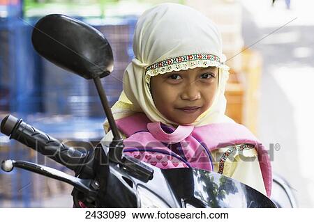 Stock Photo - Girl on a motorcycle at the bird market, Yogyakarta, Java Island, Indonesia. Fotosearch