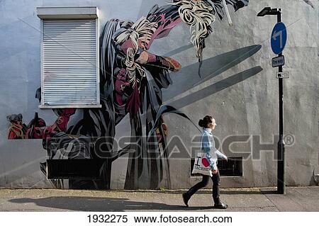 Stock Photography - Girl Passing By A Graffitti In East London, London, Uk. Fotosearch