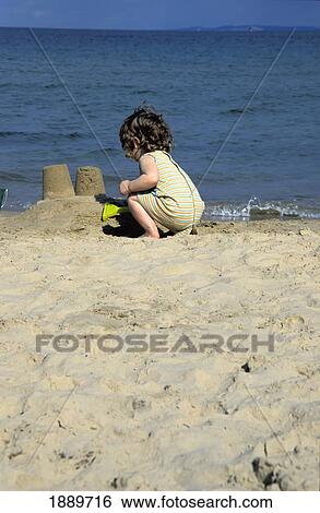 Stock Photograph - Girl Playing On The Beach Making Sandcastles. Fotosearch
