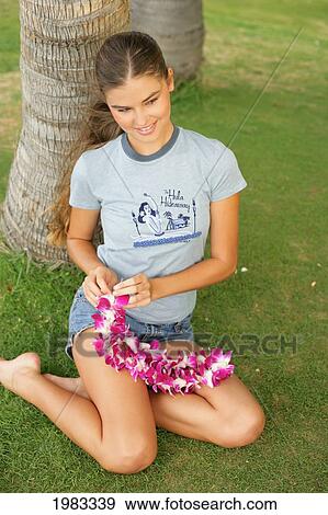 Girl Sitting Beneath A Palm Tree Tying An Orchid Lei. View Large Photo Image Stock Photo - Girl Sitting Beneath A Palm Tree Tying An Orchid Lei.. Fotosearch