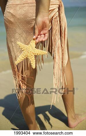 Picture - Girl Standing On Tropical Beach Wearing Pareo, Holding A Starfish, Legs And Torso. Fotosearch