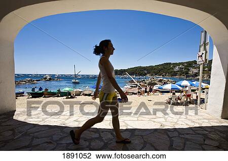 Stock Image - Girl Walking Under Arch Near Beach In Calella Fishing Village. Fotosearch