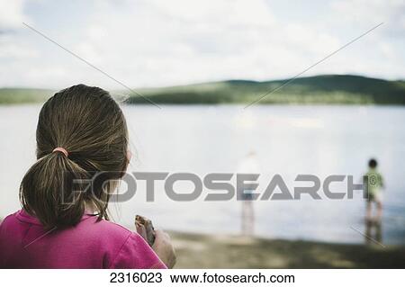 Stock Image - Girl With Ponytail Eating A Granola Bar And Gazing At A Lake; Thetford Mines Quebec Canada. Fotosearch
