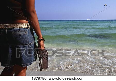 Stock Photograph - Girl With Sandals Standing On The Beach, Cyprus. Fotosearch