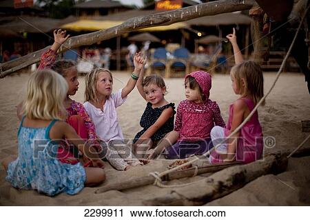 Stock Image - Girls chat together in the shade of a traditional fishing boat in front of beach side restuarants, Patnum Beach, Goa, India.. Fotosearch