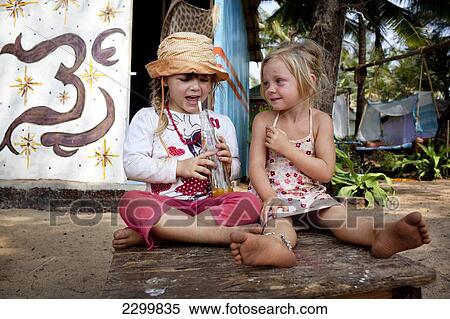 Stock Photography - Girls drink juice though a straw sat on a table, Patnum, Goa, India.. Fotosearch