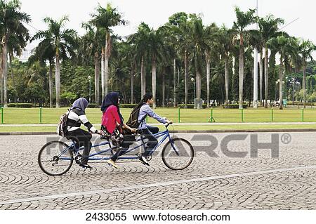 Stock Photography - Girls on a bicycle on Merdeka Square, Jakarta, Java, Indonesia. Fotosearch