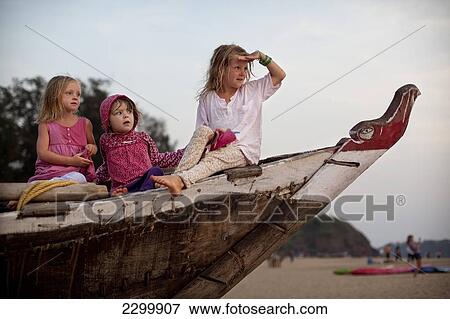 Stock Photo - Girls play together on a traditional fishing boat on holiday in India, Patnum Beach, Goa, India.. Fotosearch