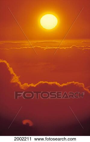 Stock Image - Glowing Yellow Sun Ball, Bright Orange Sunset Skies Above Cumulus Clouds. Fotosearch