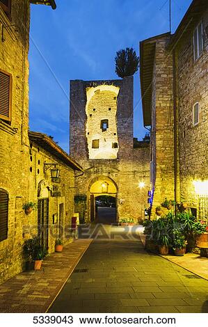 Stock Image - Golden lights illuminate historic buildings and walkway; Assisi, Umbria, Italy. Fotosearch