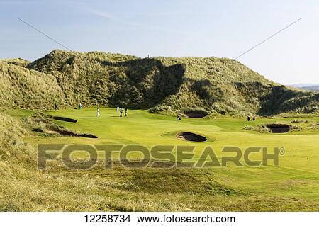 Golfers on green framed by grassy hills with blue sky; County Clare, Ireland View Large Photo Image Picture - Golfers on green framed by grassy hills with blue sky; County Clare, Ireland. Fotosearch