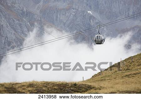 Stock Photo - Gondola going up cable with clouds in the valley and mountain slope in the background; Finkenberg, Austria. Fotosearch