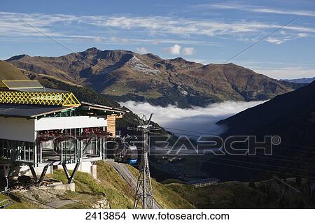 Gondola with tower and cables leaving building with clouds in the valley and mountains; Hintertux, Austria View Large Photo Image Picture - Gondola with tower and cables leaving building with clouds in the valley and mountains; Hintertux, Austria. Fotosearch