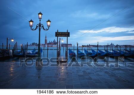 Gondolas Moored Along The Water's Edge And The Street Lights Illuminated; Venice Venezia Italy View Large Photo Image Stock Photograph - Gondolas Moored Along The Water's Edge And The Street Lights Illuminated; Venice Venezia Italy. Fotosearch