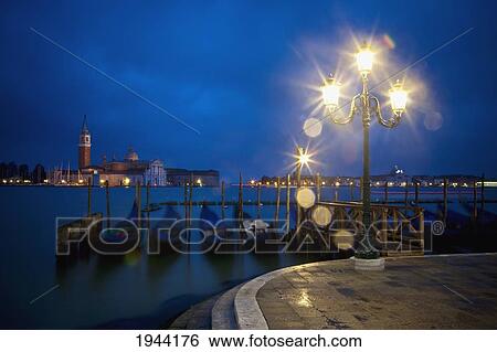 Stock Photograph - Gondolas Moored By A Wooden Pier With A Light At Dusk; Venice Venezia Italy. Fotosearch
