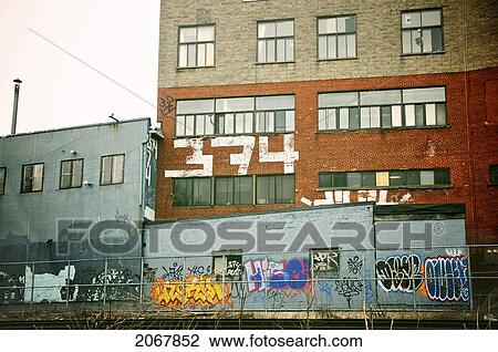 Stock Image - Graffiti On Old Industrial Building Behind Steel Fence, Montreal, Quebec. Fotosearch