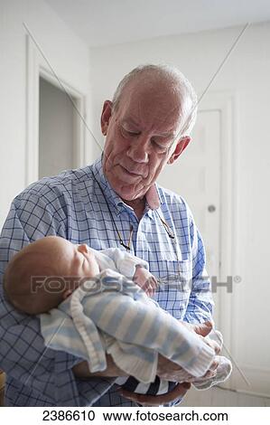 Stock Image - Grandfather holding sleeping newborn in his arms and gazing admiringly; Toronto, Ontario, Canada. Fotosearch